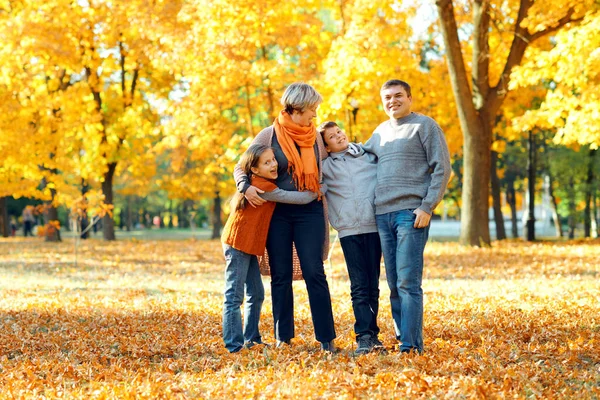 Familia feliz posando, jugando y divirtiéndose en el parque de otoño de la ciudad. Los niños y los padres juntos tienen un buen día. Luz del sol brillante y hojas amarillas en los árboles, temporada de otoño . — Foto de Stock