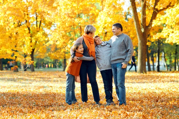 Bonne famille posant, jouant et s'amusant dans le parc de la ville d'automne. Enfants et parents passent une bonne journée ensemble. Lumière du soleil vive et feuilles jaunes sur les arbres, saison automnale . — Photo