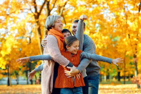 Szczęśliwa rodzina pozowanie, gry i zabawy w jesiennym parku miejskim. Dzieci i rodzice razem o miłym dniu. Jasne światło słoneczne i żółte liście na drzewach, jesień sezonu. — Zdjęcie stockowe