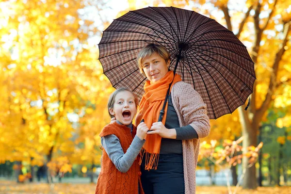 Familia feliz posando bajo el paraguas, jugando y divirtiéndose en el parque de otoño de la ciudad. Los niños y los padres juntos tienen un buen día. Luz del sol brillante y hojas amarillas en los árboles, temporada de otoño . — Foto de Stock