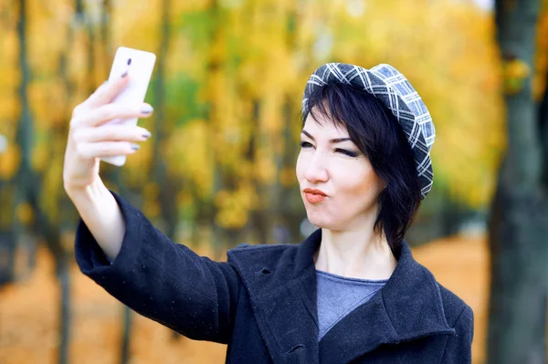 Mulher bonita tirando selfie por smartphone e se divertindo no parque da cidade de outono, temporada de outono, folhas amarelas — Fotografia de Stock