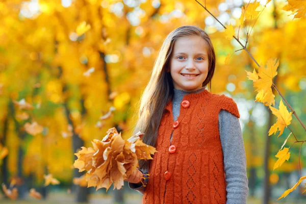 Porträtt av Happy Girl i höst stadsparken. Poserar med bukett gula blad. Starkt solljus och gyllene träd, höstsäsongen. — Stockfoto