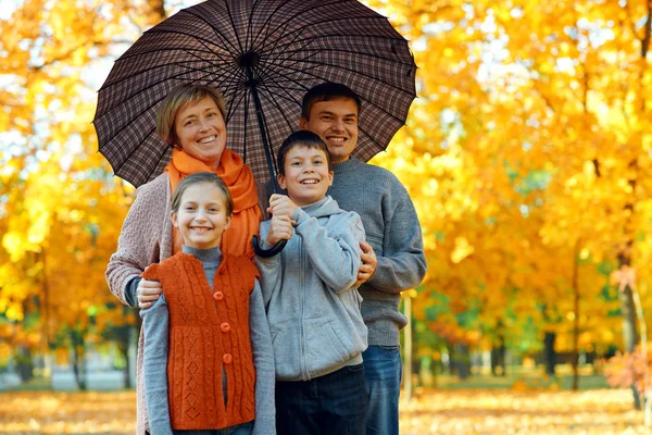 快乐的家庭在伞下摆姿势，在秋天的城市公园里玩耍和玩耍。孩子和父母一起度过了愉快的一天。明亮的阳光和黄叶在树上，秋天的季节. — 图库照片