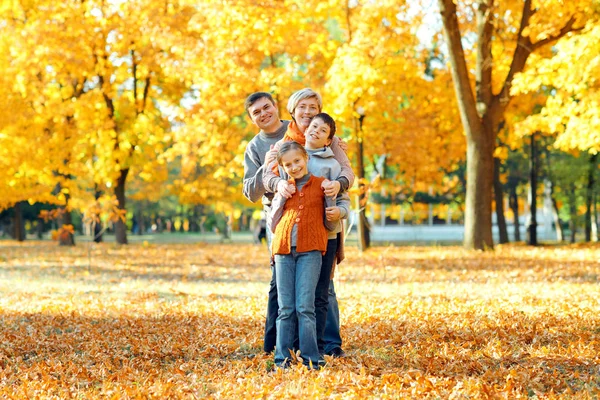 Bonne famille posant, jouant et s'amusant dans le parc de la ville d'automne. Enfants et parents passent une bonne journée ensemble. Lumière du soleil vive et feuilles jaunes sur les arbres, saison automnale . — Photo