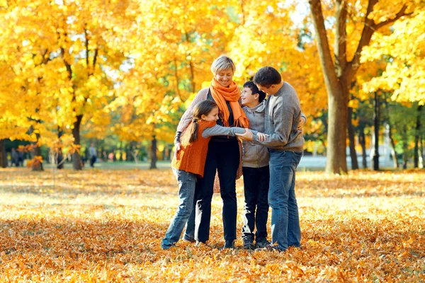 Familia feliz posando, jugando y divirtiéndose en el parque de otoño de la ciudad. Los niños y los padres juntos tienen un buen día. Luz del sol brillante y hojas amarillas en los árboles, temporada de otoño . — Foto de Stock