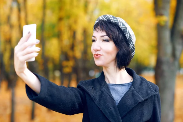 Mulher bonita tirando selfie por smartphone e se divertindo no parque da cidade de outono, temporada de outono, folhas amarelas — Fotografia de Stock