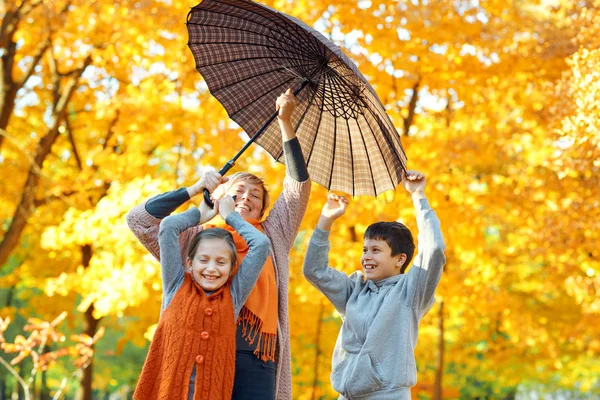 Mutlu aile şemsiye altında poz, oyun ve sonbahar şehir parkında eğlenmek. Çocuklar ve ebeveynler birlikte güzel bir gün geçiriyorlar. Ağaçlarda parlak güneş ışığı ve sarı yapraklar, sonbahar mevsimi. — Stok fotoğraf