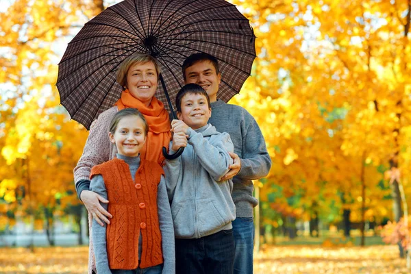 Famiglia felice in posa sotto l'ombrello, giocando e divertendosi nel parco cittadino autunnale. Bambini e genitori insieme hanno una bella giornata. Luce solare brillante e foglie gialle sugli alberi, stagione autunnale . — Foto Stock