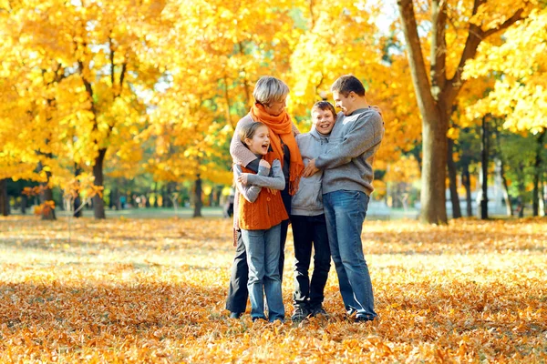 Familia feliz posando, jugando y divirtiéndose en el parque de otoño de la ciudad. Los niños y los padres juntos tienen un buen día. Luz del sol brillante y hojas amarillas en los árboles, temporada de otoño . — Foto de Stock