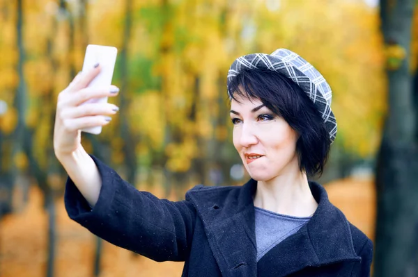 Mulher bonita tirando selfie por smartphone e se divertindo no parque da cidade de outono, temporada de outono, folhas amarelas — Fotografia de Stock