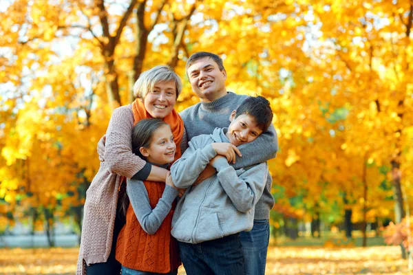 Família feliz posando, jogando e se divertindo no parque da cidade de outono. Crianças e pais juntos tendo um bom dia. Luz solar brilhante e folhas amarelas em árvores, estação de outono . — Fotografia de Stock