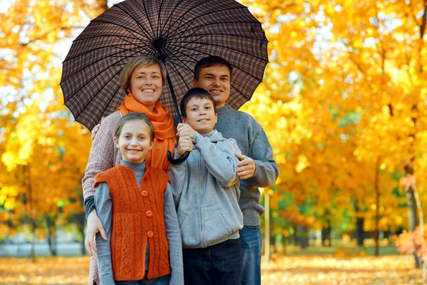 Szczęśliwa rodzina pozowanie pod parasolem, grając i zabawy w jesiennym parku miejskim. Dzieci i rodzice razem o miłym dniu. Jasne światło słoneczne i żółte liście na drzewach, jesień sezonu. — Zdjęcie stockowe