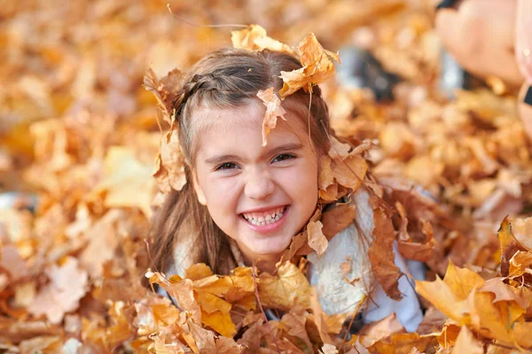 Szczęśliwe dziecko bawiąc się, stwarzając, uśmiechając się i bawiąc się w jesiennym parku miejskim. Jasne żółte drzewa i liście — Zdjęcie stockowe
