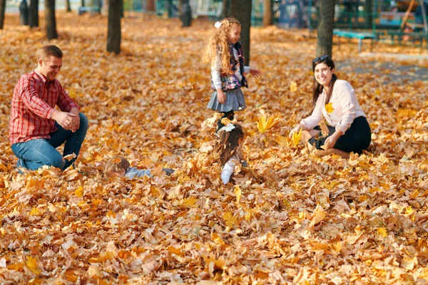 Glad familj som har semester i höstens stadspark. Barn och föräldrar poserar, ler, leker och har roligt. Ljusgula träd och blad — Stockfoto