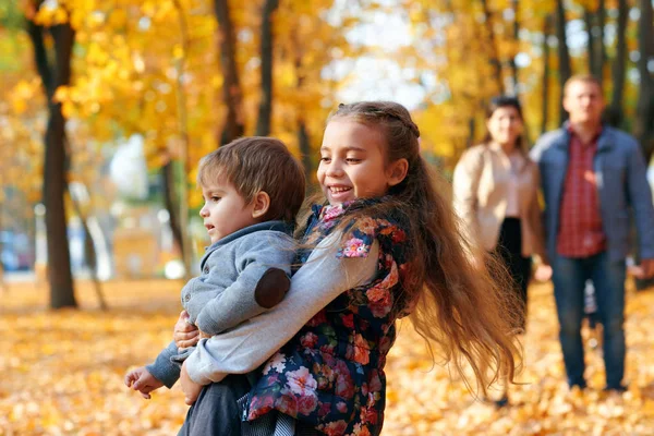 Szczęśliwy rodzina mający święto w jesienny miejski park. Dzieci i rodzice pozowanie, uśmiech, zabawy i zabawy. Jasnożółte drzewa i liście — Zdjęcie stockowe