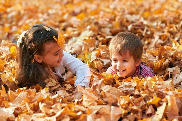 Bambini felici che giocano, posano, sorridono e si divertono nel parco cittadino autunnale. Luminosi alberi e foglie gialle — Foto Stock