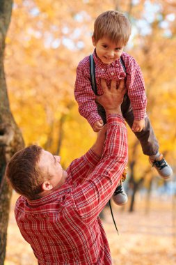 Mutlu aile sonbahar şehir parkında tatil yapıyor. Çocuklar ve ebeveynler poz veriyor, gülümsüyor, oynuyor ve eğleniyorlar. Parlak sarı ağaçlar ve yapraklar