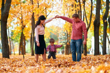 Mutlu aile sonbahar şehir parkında tatil yapıyor. Çocuklar ve ebeveynler poz veriyor, gülümsüyor, oynuyor ve eğleniyorlar. Parlak sarı ağaçlar ve yapraklar