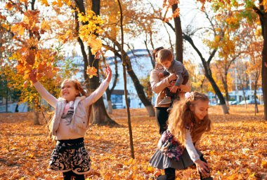 Mutlu aile sonbahar şehir parkında tatil yapıyor. Çocuklar ve ebeveynler poz veriyor, gülümsüyor, oynuyor ve eğleniyorlar. Parlak sarı ağaçlar ve yapraklar