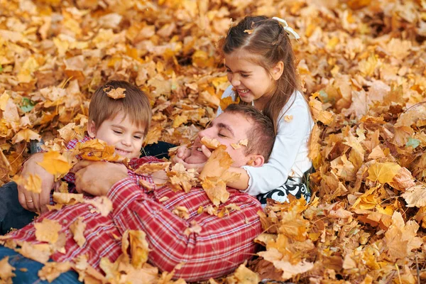 Feliz familia teniendo vacaciones en el parque de otoño de la ciudad. Niños y padres posando, sonriendo, jugando y divirtiéndose. Árboles y hojas de color amarillo brillante —  Fotos de Stock