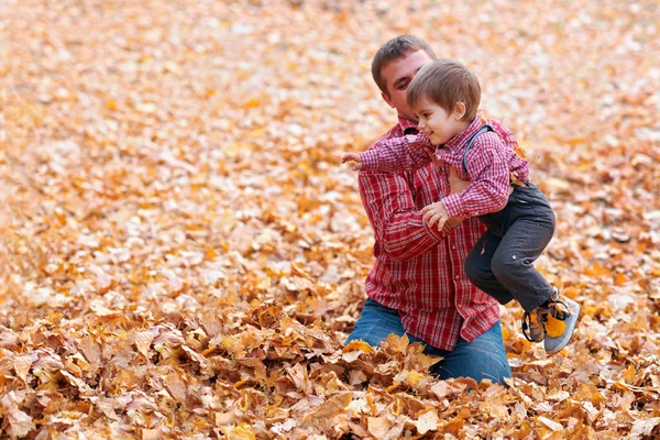 Dzieci i ojciec bawią się i mają wakacje w jesiennym parku miejskim. Pozowanie, uśmiechając się, grając i zabawy. Jasne żółte drzewa i liście — Zdjęcie stockowe