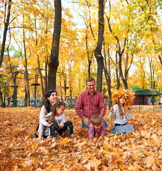 Mutlu aile sonbahar şehir parkında tatil yapıyor. Çocuklar ve ebeveynler poz veriyor, gülümsüyor, oynuyor ve eğleniyorlar. Parlak sarı ağaçlar ve yapraklar — Stok fotoğraf
