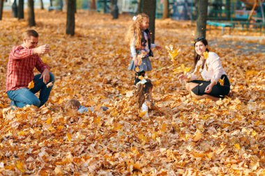 Mutlu aile sonbahar şehir parkında tatil yapıyor. Çocuklar ve ebeveynler poz veriyor, gülümsüyor, oynuyor ve eğleniyorlar. Parlak sarı ağaçlar ve yapraklar