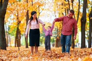 Mutlu aile sonbahar şehir parkında tatil yapıyor. Çocuklar ve ebeveynler poz veriyor, gülümsüyor, oynuyor ve eğleniyorlar. Parlak sarı ağaçlar ve yapraklar