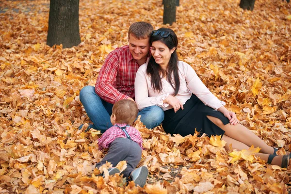 Mutlu aile sonbahar şehir parkında tatil yapıyor. Çocuklar ve ebeveynler poz veriyor, gülümsüyor, oynuyor ve eğleniyorlar. Parlak sarı ağaçlar ve yapraklar — Stok fotoğraf