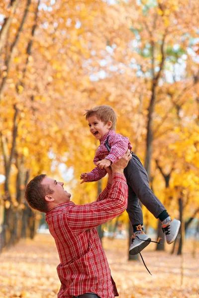 Boldog család, akik nyaralnak az őszi városi parkban. Gyerekek és szülők pózolnak, mosolyognak, játszanak és szórakoznak. Fényes sárga fák és levelek — Stock Fotó