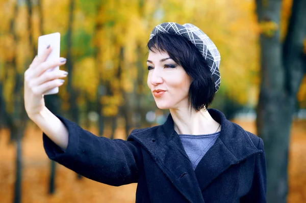 Mulher bonita tirando selfie por smartphone e se divertindo no parque da cidade de outono, temporada de outono, folhas amarelas — Fotografia de Stock