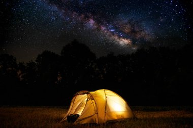 Seyahat ve kamp konsepti - yıldız dolu bir gökyüzü altında geceleri kamp çadırı. Turuncu ışıklı çadır. Güzel doğa - alan, orman, düz. Ay ve ay ışığı