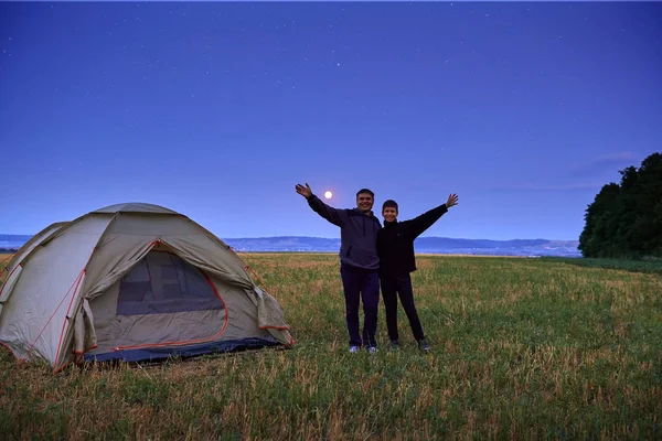 Famiglia in viaggio e in campeggio, crepuscolo, posa vicino alla tenda. Bella natura - campo, foresta, stelle e luna. Padre e figlio . — Foto Stock