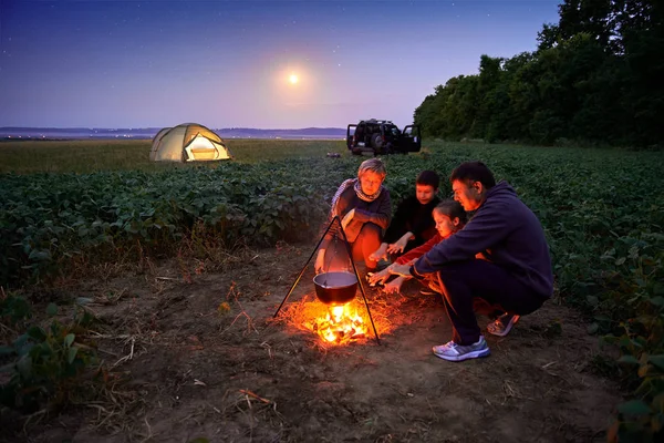 Family traveling and camping, twilight, cooking on the fire. Beautiful nature - field, forest, stars and moon. — Stock Photo, Image
