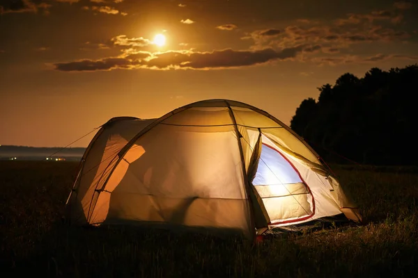 Concetto di viaggio e campeggio - tenda da campeggio di notte sotto un cielo pieno di stelle. Tenda arancione illuminata. Bella natura - campo, foresta, pianura. Luna e chiaro di luna — Foto Stock