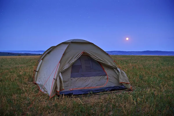 Concetto di viaggio e campeggio - paesaggio estivo e tenda, crepuscolo, luna su cielo scuro con stelle. Bella natura - campo, foresta, pianura . — Foto Stock