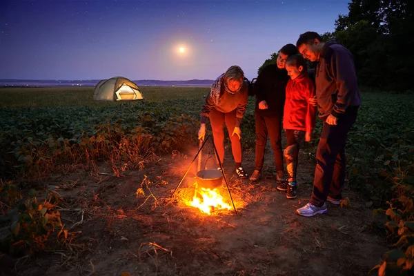 Family traveling and camping, twilight, cooking on the fire. Beautiful nature - field, forest, stars and moon. — Stock Photo, Image