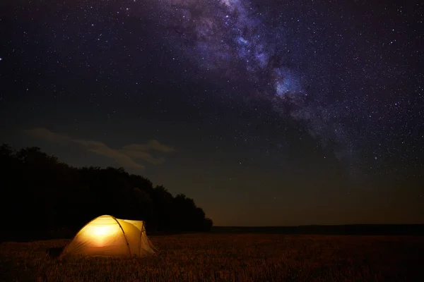 Traveling and camping concept - camp tent at night under a sky full of stars. Orange illuminated tent. Beautiful nature - field, forest, plain. Moon and moonlight — Stock Photo, Image