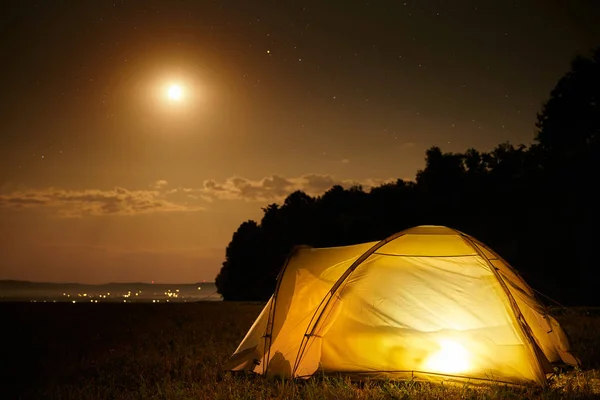 Concetto di viaggio e campeggio - tenda da campeggio di notte sotto un cielo pieno di stelle. Tenda arancione illuminata. Bella natura - campo, foresta, pianura. Luna e chiaro di luna — Foto Stock