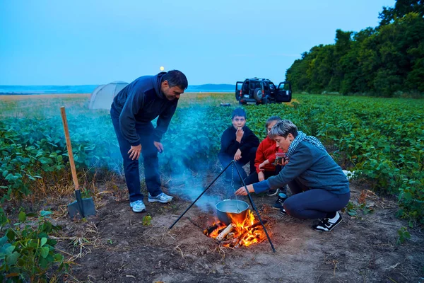 Famiglia in viaggio e in campeggio, crepuscolo, cucina sul fuoco. Bella natura - campo, foresta e luna . — Foto Stock