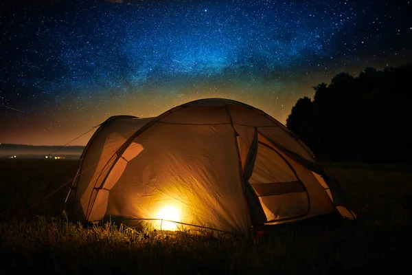 Concetto di viaggio e campeggio - tenda da campeggio di notte sotto un cielo pieno di stelle. Tenda arancione illuminata. Bella natura - campo, foresta, pianura. Luna e chiaro di luna — Foto Stock