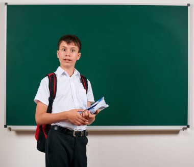 Sırt çantası ve okul malzemeleri, kara tahta arka plan ile poz bir okul çocuğun portresi - geri okul ve eğitim kavramı