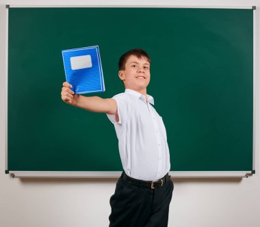 Bir okul çocuğunun kara tahta arka plan üzerinde mavi egzersiz kitabı ile poz portresi - geri okul ve eğitim kavramı