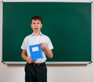 Bir okul çocuğunun kara tahta arka plan üzerinde mavi egzersiz kitabı ile poz portresi - geri okul ve eğitim kavramı