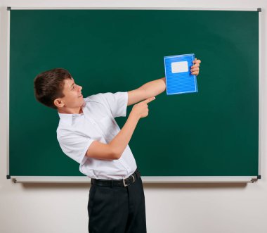 Bir okul çocuğunun kara tahta arka plan üzerinde mavi egzersiz kitabı ile poz portresi - geri okul ve eğitim kavramı