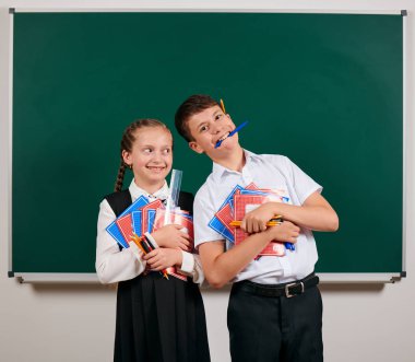 Bir okul çocuğu ve kız öğrenci portresi egzersiz kitapları, kalemler, kalemler ve kara tahta arka plan üzerinde diğer okul malzemeleri ile poz - geri okul ve eğitim kavramı