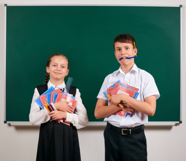 Bir okul çocuğu ve kız öğrenci portresi egzersiz kitapları, kalemler, kalemler ve kara tahta arka plan üzerinde diğer okul malzemeleri ile poz - geri okul ve eğitim kavramı