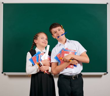 Bir okul çocuğu ve kız öğrenci portresi egzersiz kitapları, kalemler, kalemler ve kara tahta arka plan üzerinde diğer okul malzemeleri ile poz - geri okul ve eğitim kavramı