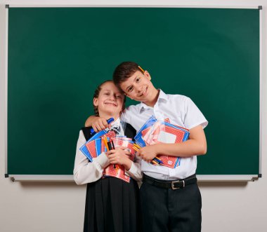 Bir okul çocuğu ve kız öğrenci portresi egzersiz kitapları, kalemler, kalemler ve kara tahta arka plan üzerinde diğer okul malzemeleri ile poz - geri okul ve eğitim kavramı