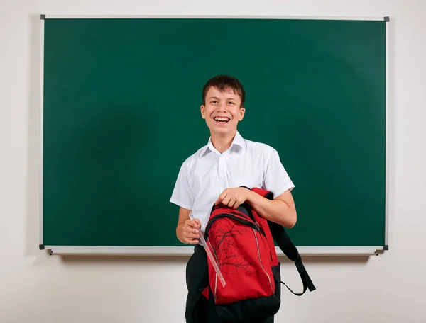 Porträt eines Schuljungen auf der Suche nach Schulmaterial im Rucksack, Tafel-Hintergrund - zurück zu Schule und Bildungskonzept — Stockfoto